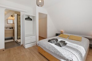 Un dormitorio con cama, mesita de noche, lámpara, armario y baño visible a través de una puerta abierta.