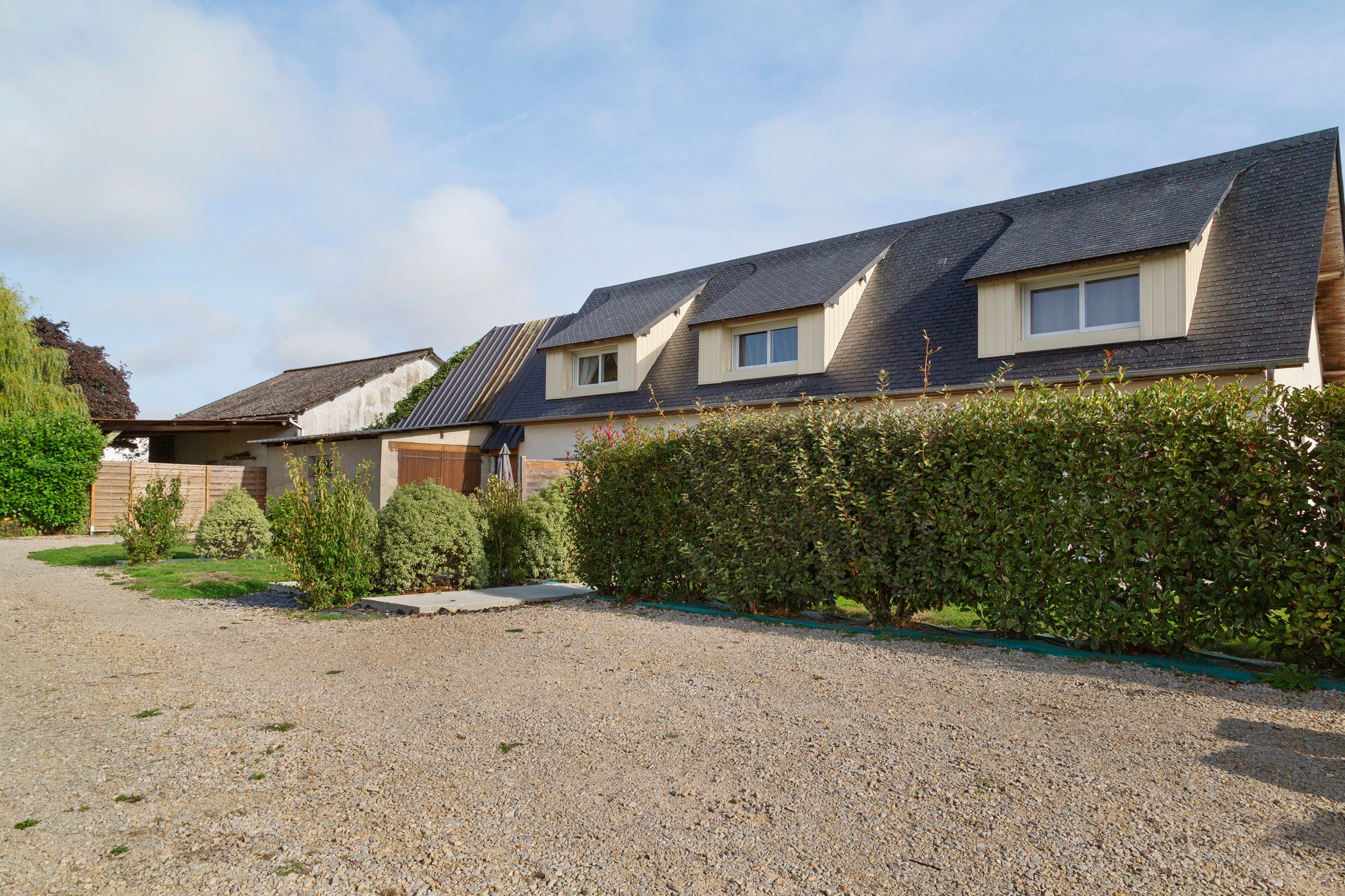 A row of houses with pitched roofs, a gravel driveway, and a hedge in the foreground.