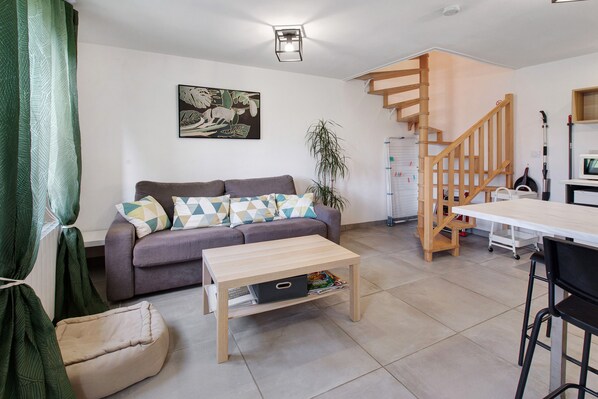 A living room with a sofa, coffee table, and a staircase leading to an upper level. - 2-Star Holiday Home “Le Mascaret des Abbayes du Val de Seine” (Sainte-Marguerite-sur-Duclair)