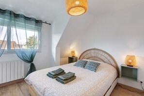 A bedroom with a bed, two bedside lamps, a window with sheer curtains, and a hanging light fixture. - 2-Star Holiday Home “Le Mascaret des Abbayes du Val de Seine” (Sainte-Marguerite-sur-Duclair)