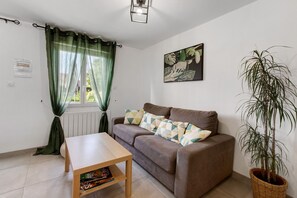 Una sala de estar con sofá, una mesita, una planta en maceta y una ventana con cortinas.