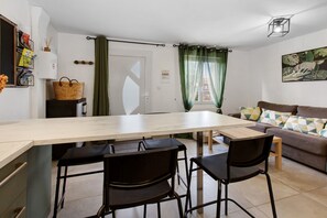 Eine moderne Küche mit einer großen Kochinsel, schwarzen Stühlen, einer Couch mit gemusterten Kissen und einem grünen Vorhang.