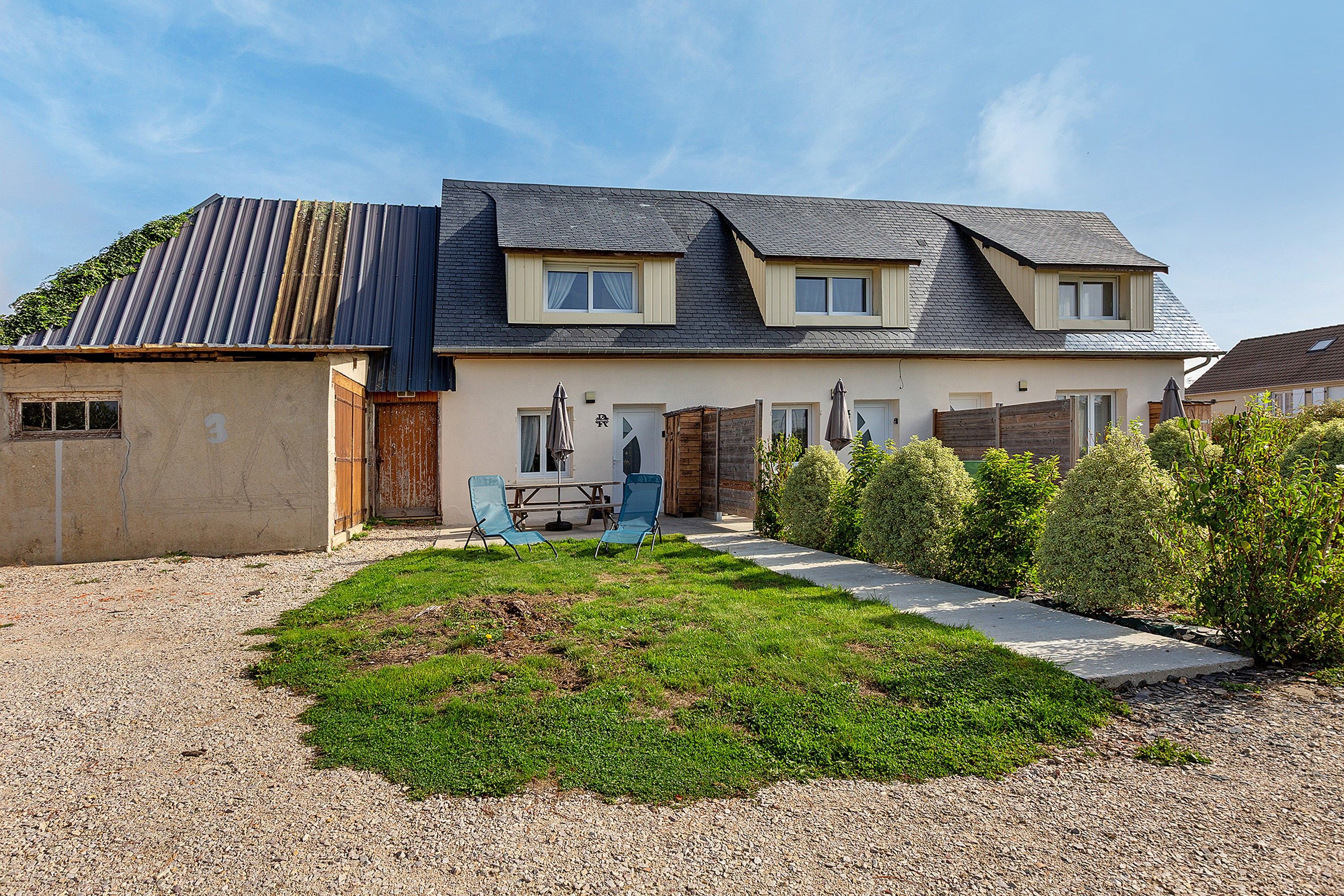 A two-story house with a sloped roof, a front porch with a table and chairs, and a well-maintained lawn.