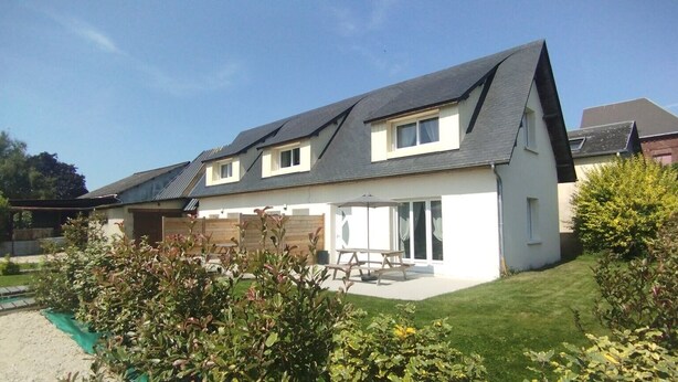 A two-story house with a sloped roof, a patio with a table and chairs, and a garden with various plants. - 2-Star Holiday Home “Le Mascaret des Abbayes du Val de Seine” (Sainte-Marguerite-sur-Duclair)