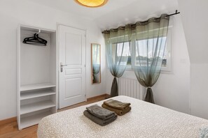 A bedroom with a bed, a wardrobe, a window with sheer curtains, and a view of the outdoors. - 2-Star Holiday Home “Le Mascaret des Abbayes du Val de Seine” (Sainte-Marguerite-sur-Duclair)