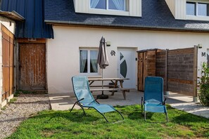 Una casa con un patio que tiene dos sillas azules, una mesa y una sombrilla.