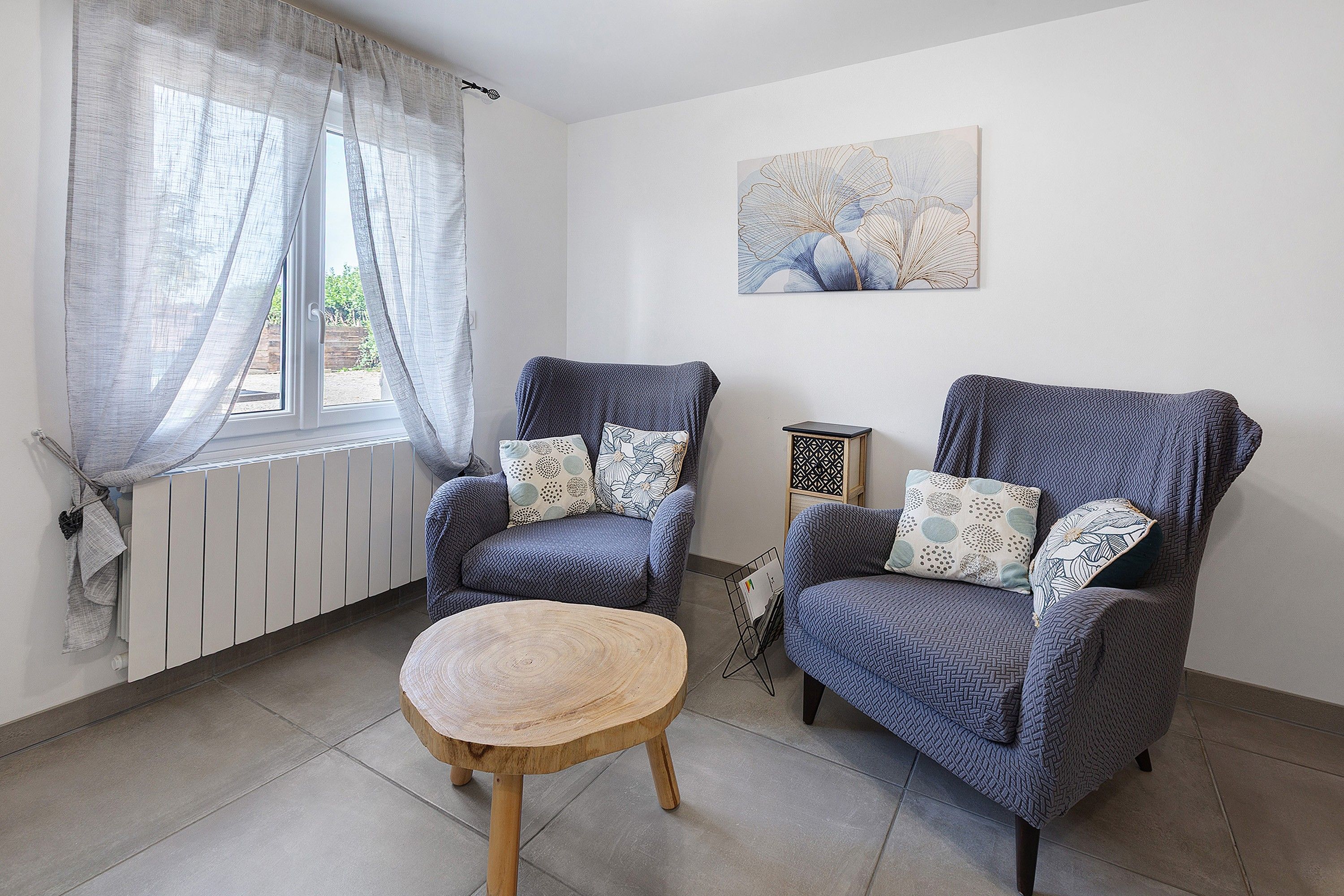 Une pièce avec deux fauteuils, une petite table en bois et un radiateur.