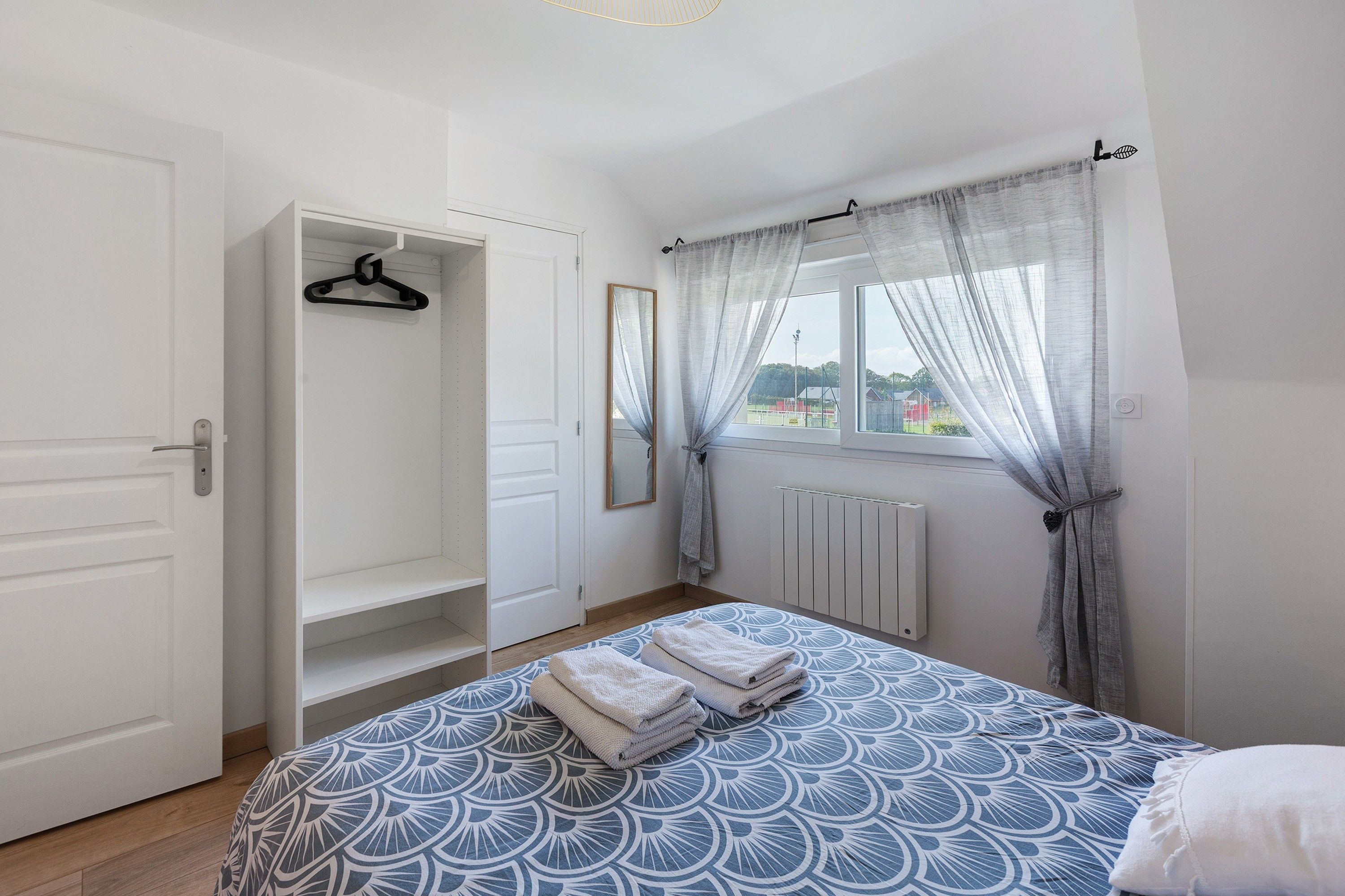 Een slaapkamer met een bed, een kledingkast, een radiator en een raam met gordijnen.