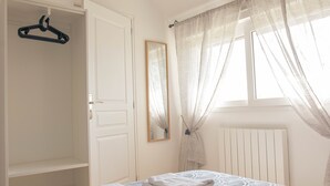 Une chambre à coucher avec un lit, un porte-manteau suspendu, un miroir et une fenêtre avec des rideaux.