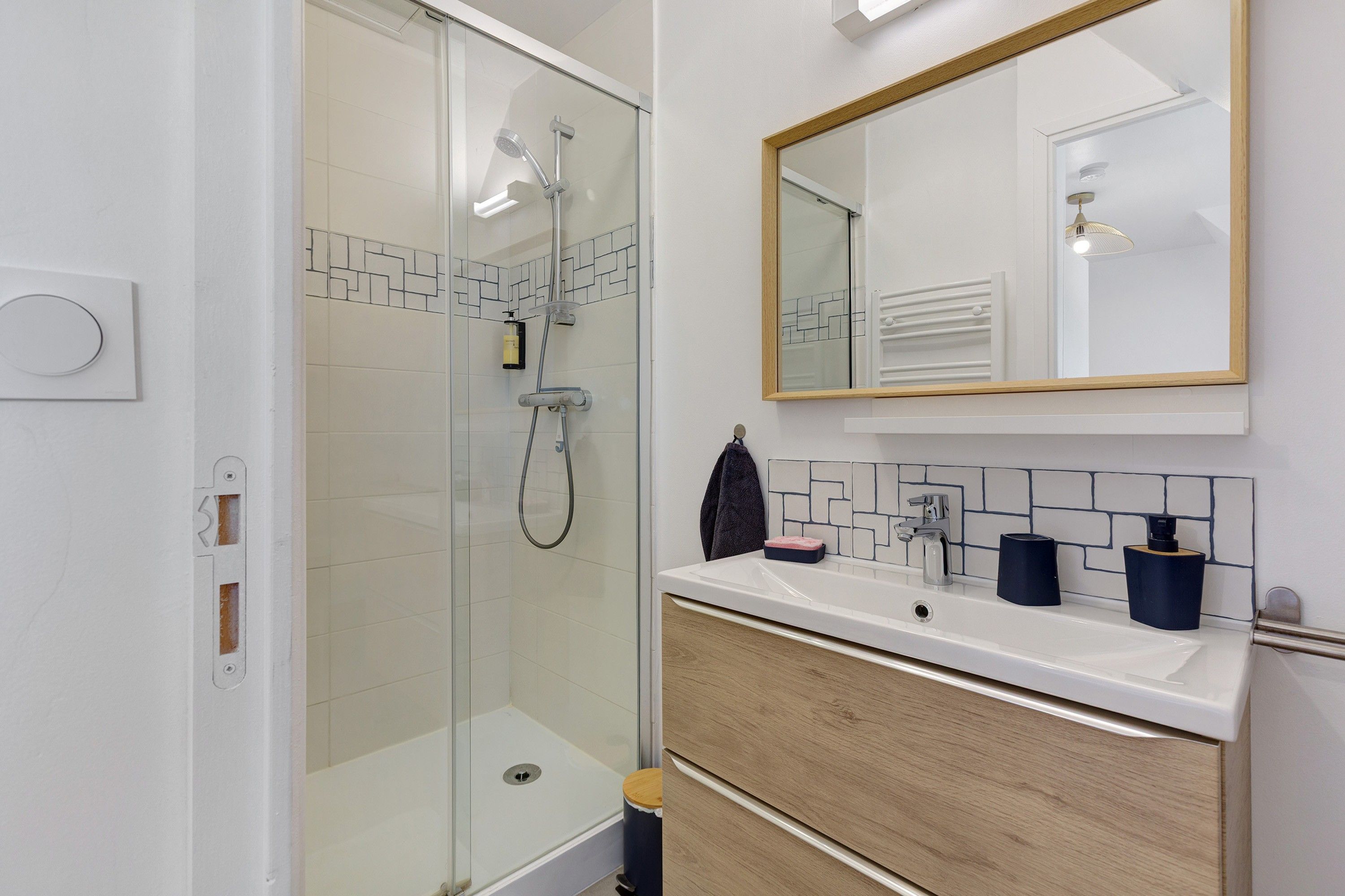 Een moderne badkamer met een douchecabine van glas, een houten wastafelmeubel en een spiegel boven de wastafel.