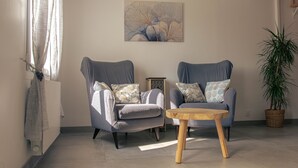 Un salon avec deux fauteuils, une table basse en bois, une œuvre d’art accrochée au mur et une plante en pot.