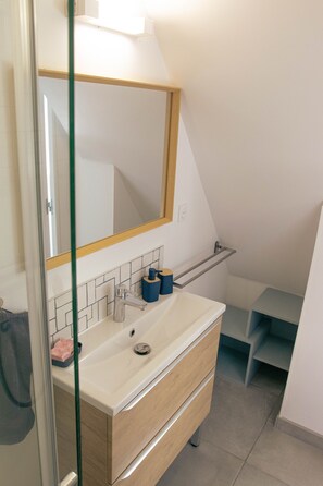 Un baño con lavamanos blanco, espejo y toallero.