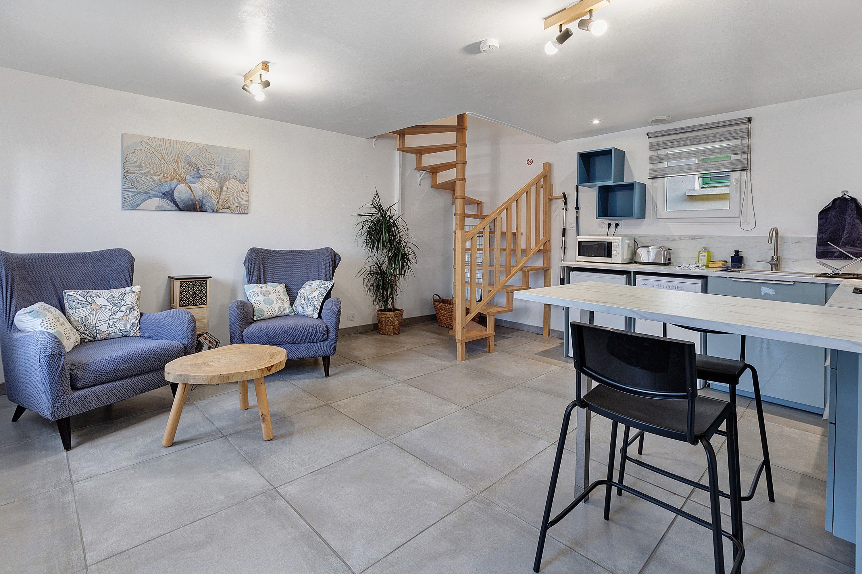 Un espacio habitable moderno con sofá, una mesa de comedor con sillas, zona de cocina y una escalera de madera.