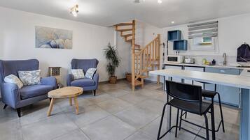 Un espacio habitable moderno con sofá, una mesa de comedor con sillas, zona de cocina y una escalera de madera.