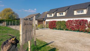 Un bâtiment avec une allée de gravier, une enseigne en bois et un espace clôturé où se trouve une chèvre.