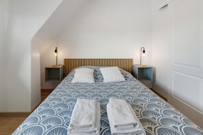 Una cama bien hecha con una colcha estampada, dos almohadas y dos toallas dobladas.