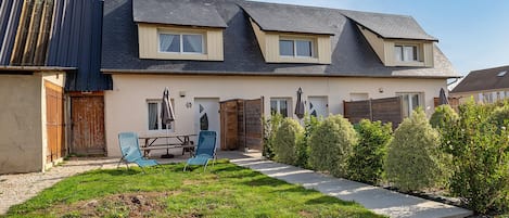 A two-story house with a sloped roof, a patio with a table and chairs, and a well-maintained lawn.