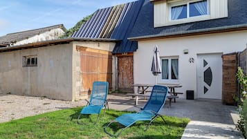 Ein Haus mit einer Terrassenanlage, ausgestattet mit zwei blauen Liegestühlen und einem Picknicktisch.