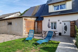 Ein Haus mit einer Terrassenanlage, ausgestattet mit zwei blauen Liegestühlen und einem Picknicktisch.