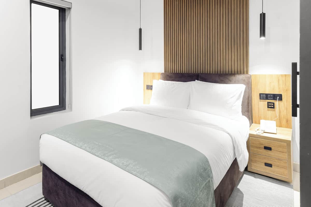 A modern hotel room with a bed, bedside table, and a window.