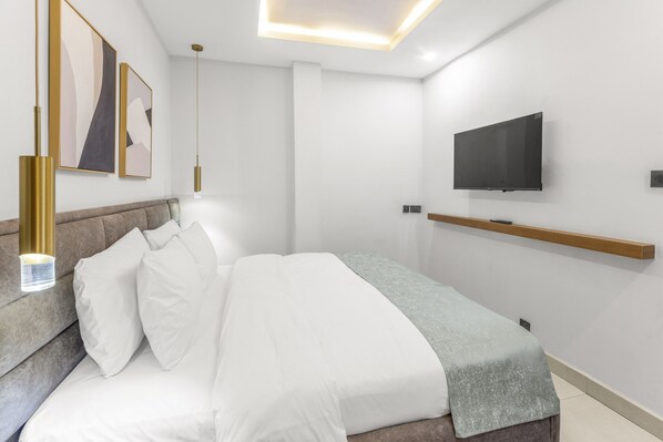 A modern bedroom with a bed, a mounted TV, and a bedside table. - Tide Hotels and Resorts (Abuja)