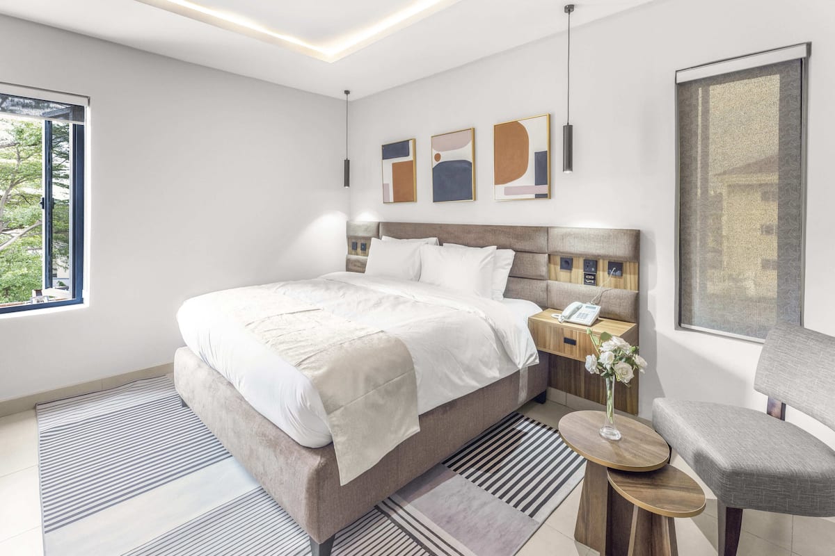 A modern hotel room with a large bed, bedside tables, a chair, and artwork on the walls.