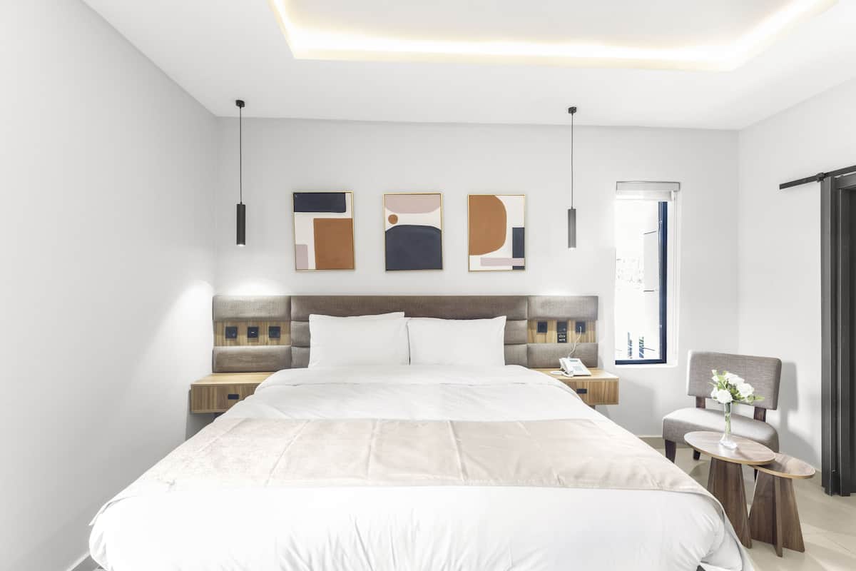 A modern hotel room with a large bed, bedside tables, a chair, and artwork on the wall.