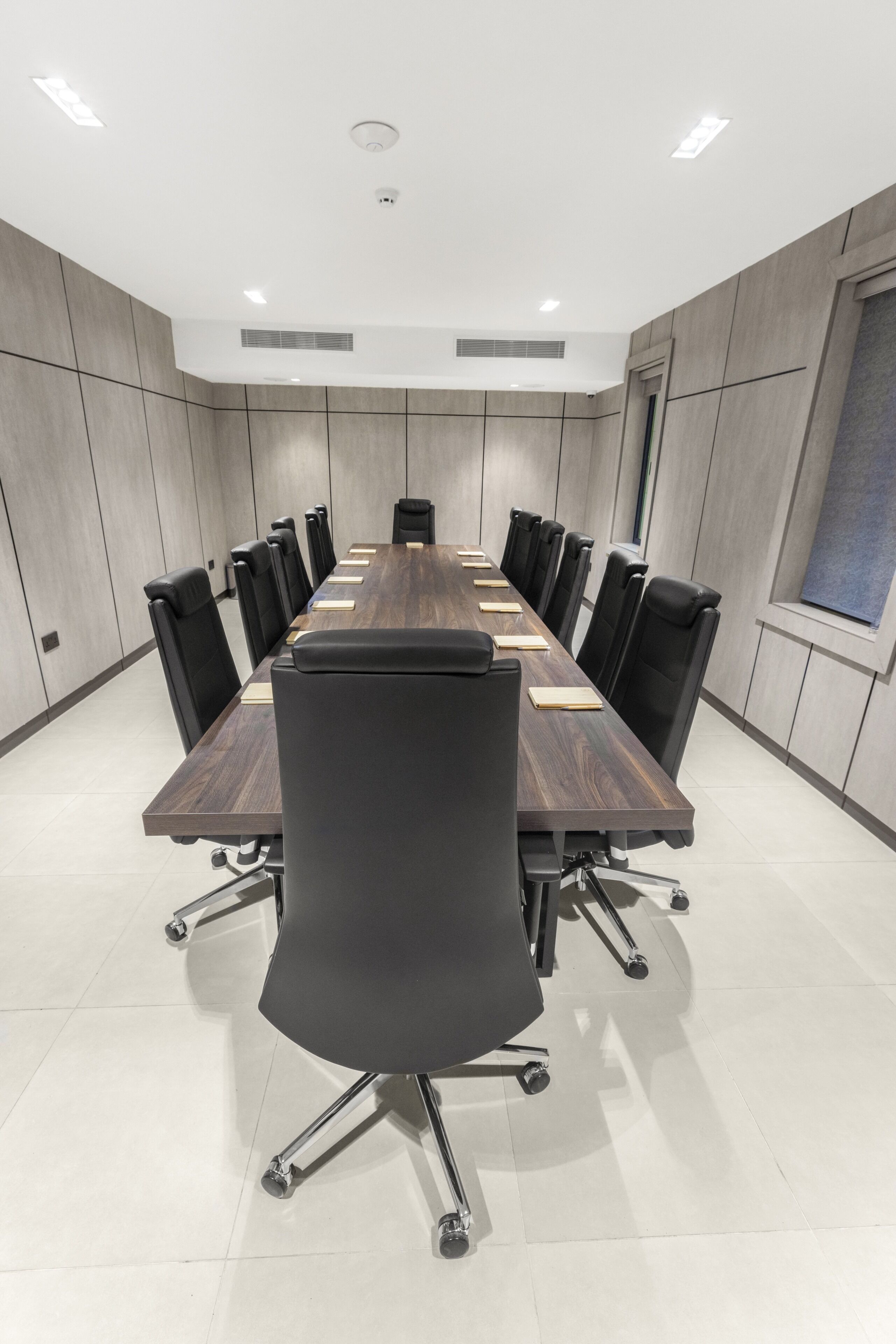 Une salle de conférence avec une longue table, des chaises noires et un plafond blanc.