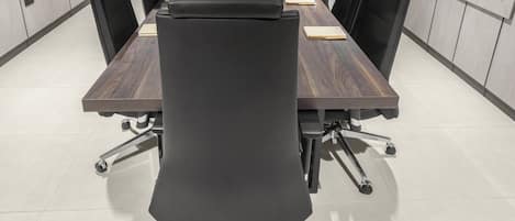 Une salle de conférence avec une longue table, des chaises noires et un plafond blanc.