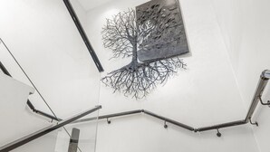 Een moderne trap met glazen balustrades, een geometrische lamp en een abstract kunstwerk van een boom aan de muur.