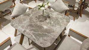 Een moderne eetruimte met marmeren tafels, beklede stoelen en bloemstukken.
