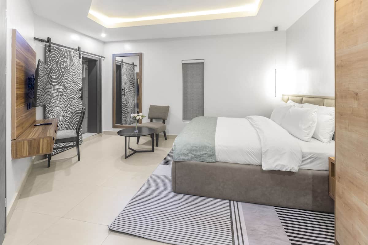 A modern bedroom with a bed, a chair, a small table, and a mirror.