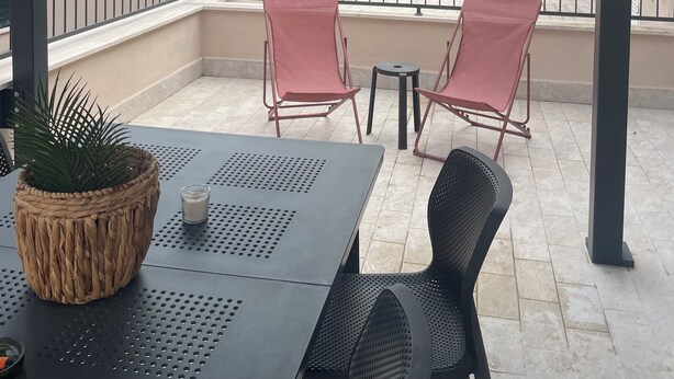 Un espacio de estar al aire libre con techo, una mesa, dos sillas y una planta en maceta.
