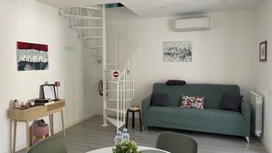 Un espacio habitable moderno con una escalera en espiral, un sofá verde, una mesa de comedor con un centro de mesa con planta y una pequeña mesita auxiliar.