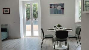 Un comedor moderno con una mesa redonda, cuatro sillas, una lámpara en el techo y vistas al balcón exterior a través de un ventanal.