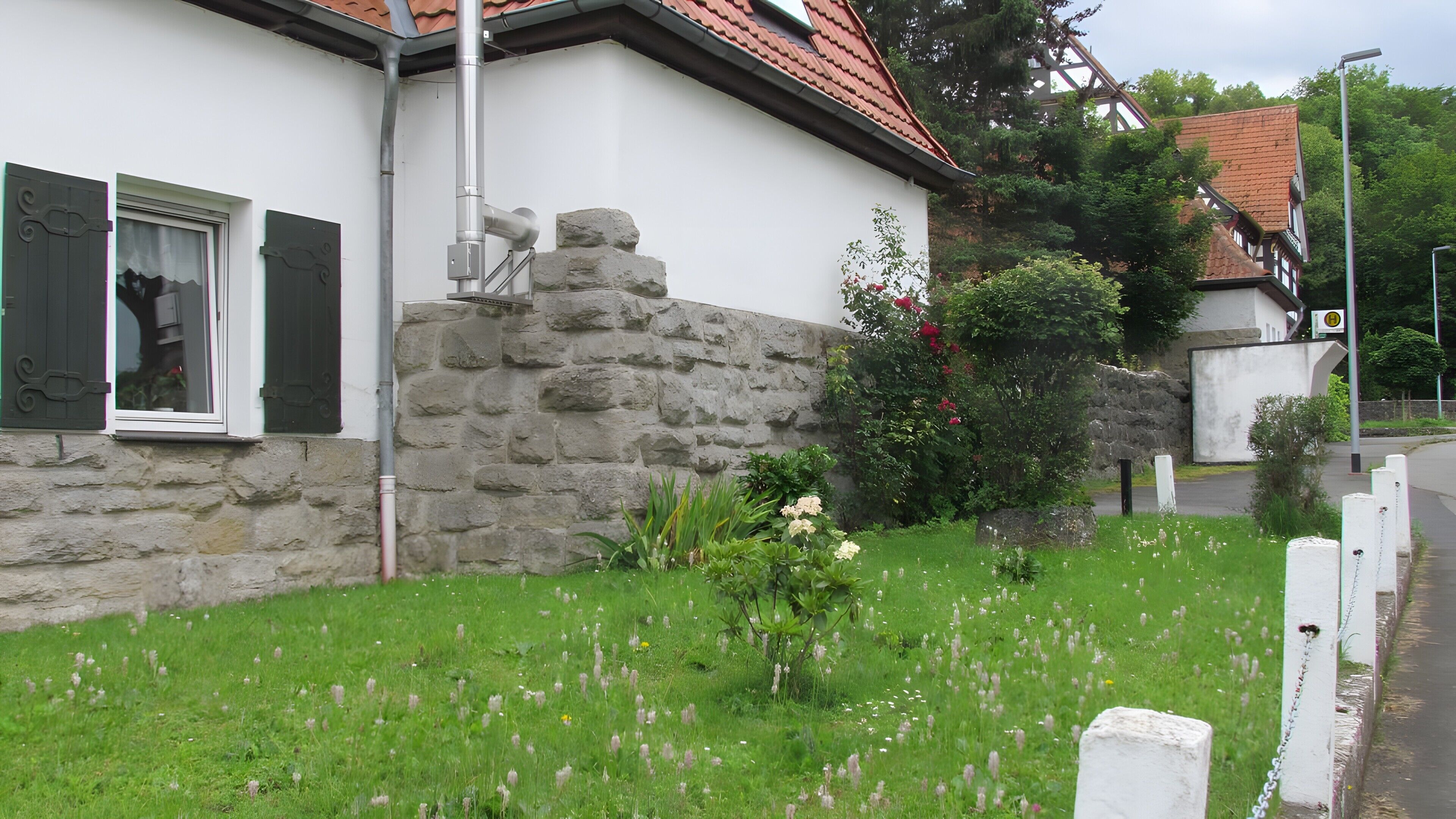 A house with a stone wall, a window with shutters, and a garden with flowers.