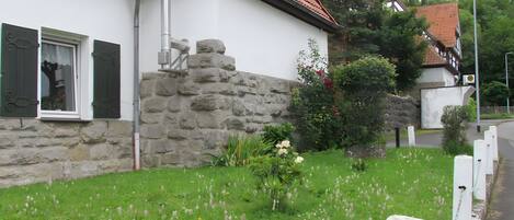 A house with a stone wall, a window with shutters, and a garden with flowers.