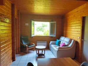 L’intérieur d’un chalet en bois, avec un canapé, un fauteuil, une petite table et une fenêtre donnant sur un paysage verdoyant.