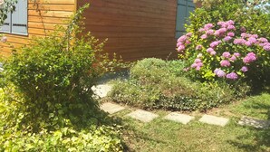 Uma casa de madeira com telhado de cerâmica, rodeada por vegetação e plantas floridas.