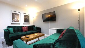 Una sala de estar con un sofá verde, una mesa de centro y un televisor de pantalla plana montado en la pared.