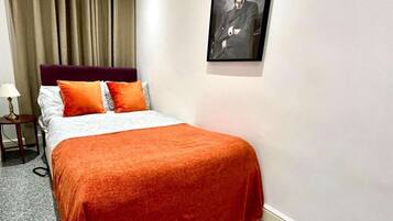 Habitación de hotel con cama, mesita de noche, lámpara, un cuadro enmarcado en la pared y ventana con cortinas.