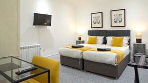 Una cama doble con dos almohadas, una mesita de noche con lámpara, un televisor montado en la pared y una mesa de cristal con un control remoto.