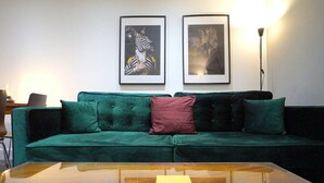 Un sofá verde con un cojín rojo, una mesa de centro con un libro, y dos cuadros en la pared.