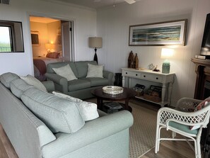 A living room with a sofa, a chair, a small table, a lamp, a painting, and a fireplace. - Oceanfront 3BR/2BA Camelot, Ocean City, MD w/  Balcony Views, Pool & Beach Access (Ocean City)