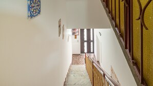 Una escalera con suelo de mármol que conduce a una puerta, una pared con un plato decorativo y una barandilla con una pared amarillenta a un lado.