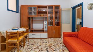 Un espacio habitable pequeño con una mesa de comedor, sillas, un sofá, un armario de madera con puertas de cristal y un suelo estampado.