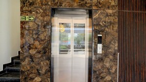 An elevator with a fire exit sign, marble walls, and a control panel. - Super Townhouse Mahamrityunjay Dwar (Ujjain)