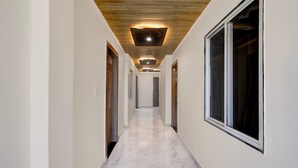 A hallway with wooden ceiling panels, recessed lighting, and a large window on the right. - Super Townhouse Mahamrityunjay Dwar (Ujjain)