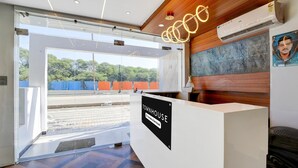 A reception desk with a sign reading 'TOWNHOUSE & Company-Service,' a glass door leading outside, and a view of trees through the glass. - Super Townhouse Mahamrityunjay Dwar (Ujjain)