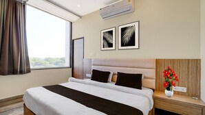 A hotel room with a bed, a nightstand, a vase with flowers, and two framed leaf designs on the wall. - Super Townhouse Mahamrityunjay Dwar (Ujjain)
